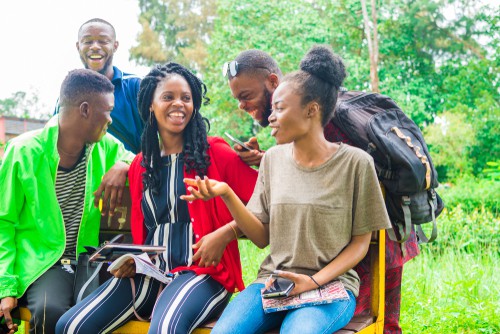 groupe de jeunes amis africains qui traînent ensemble dehors sur un banc et rient en discutant